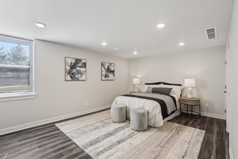 Blue Springs, MO Townhomes - Chapman Ridge Townhomes - A Bedroom With Queen-Sized Bed, Abstract Wall Art, Vinyl Plank Flooring, Matching Bedside Lamps, And A Large Window.