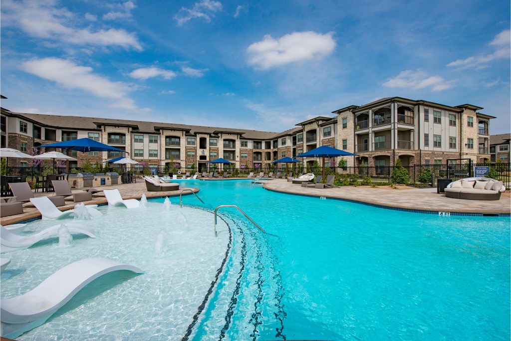 a large swimming pool with chairs and umbrellas in front of an apartment building