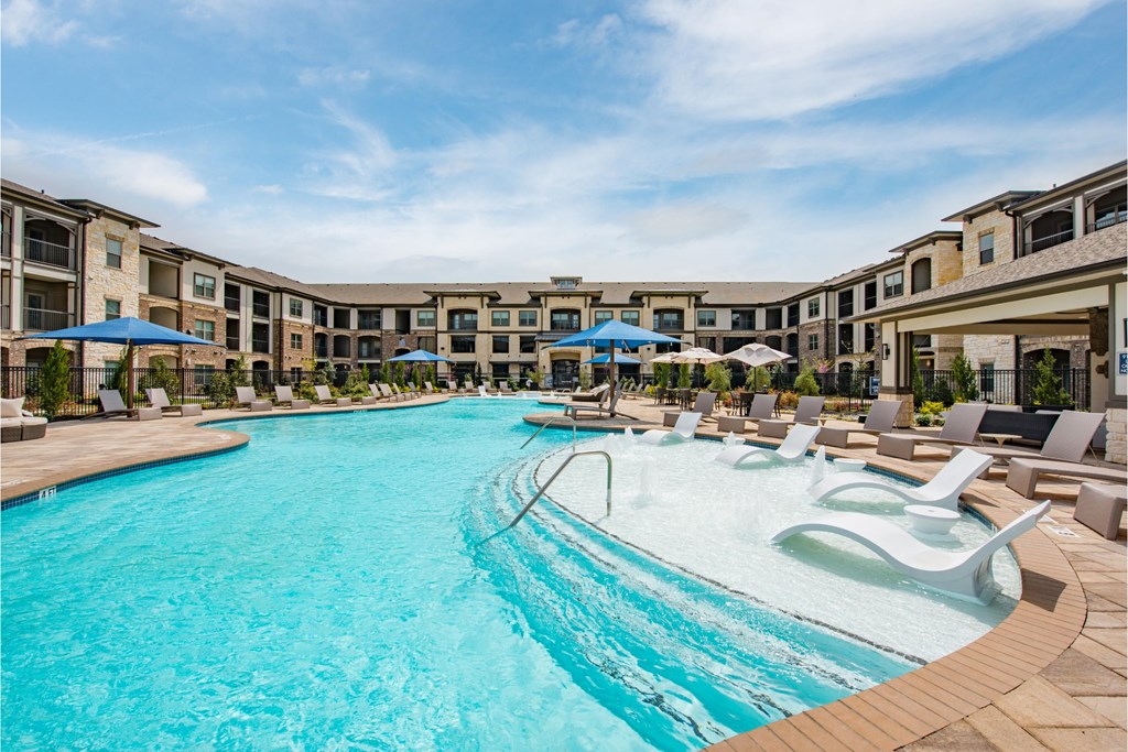 a large swimming pool with lounge chairs and umbrellas in front of a hotel