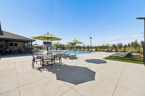 A pool area with a table and chairs and umbrellas.