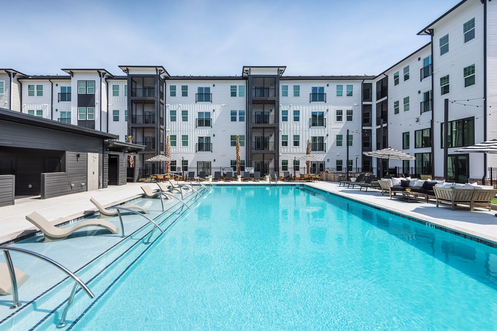A large swimming pool with sun loungers in front of apartment buildings.
