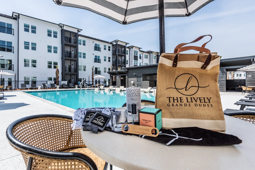 A bag with "The Lively Grande Dunes" written on it is on a table next to a pool.