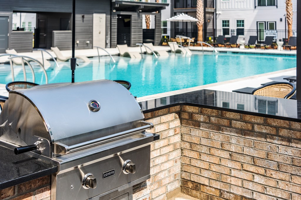 A grill is on a brick wall next to a pool.