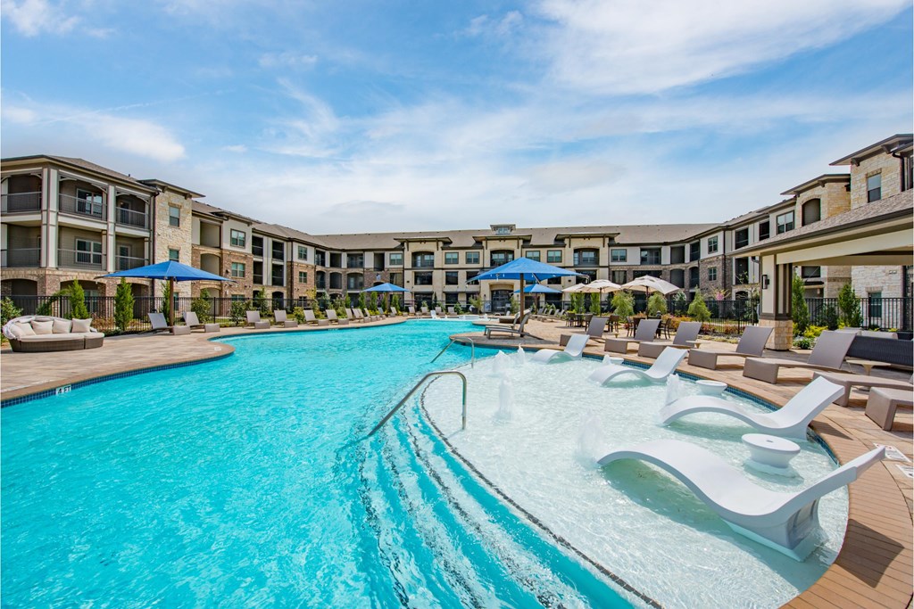 a large swimming pool with lounge chairs and umbrellas in front of a hotel