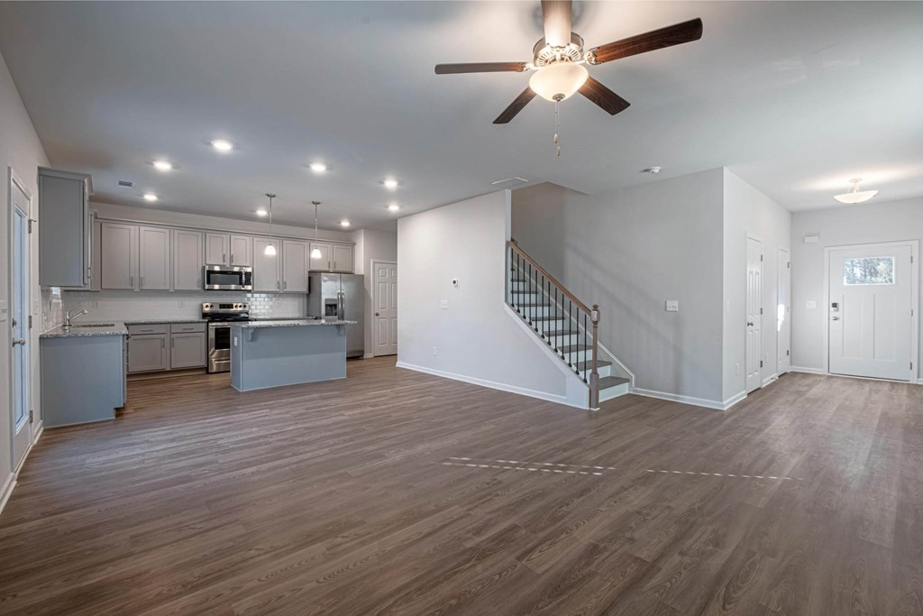 an empty living room with a ceiling fan and a kitchen