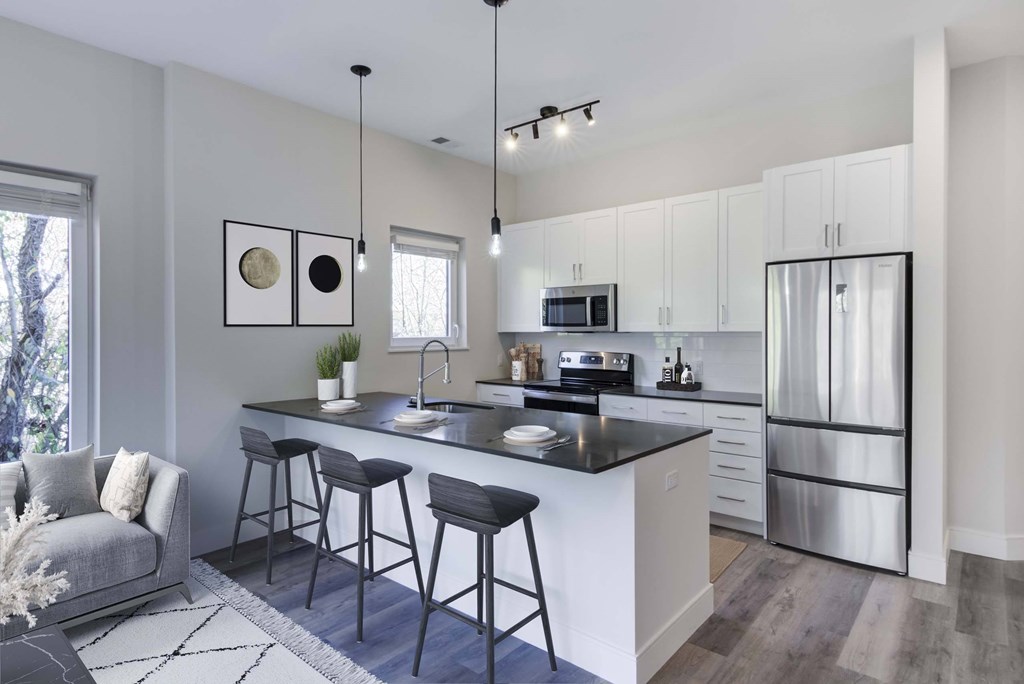 The Beacon furnished apartment kitchen with white cabinets, a peninsula style black countertop with bar stool overhang, wood flooring, and stainless steel appliances