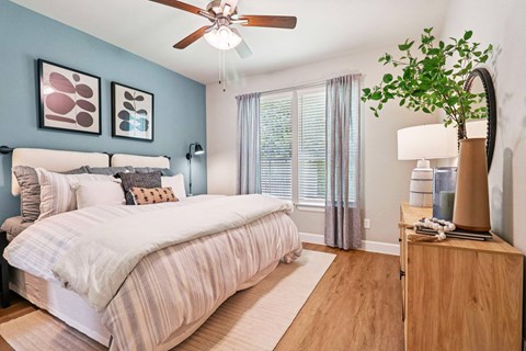 A bedroom with a bed, a ceiling fan, and a nightstand with a plant on it.