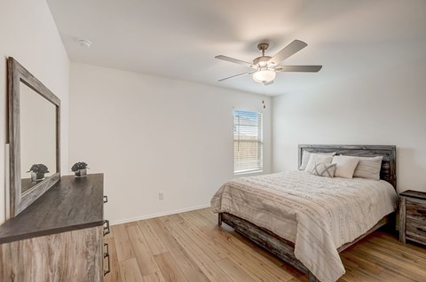 Rustic bedroom featuring warm hardwood floors, with a small window strategically placed next to the bed for natural light, and enhanced ventilation provided by a ceiling fan.