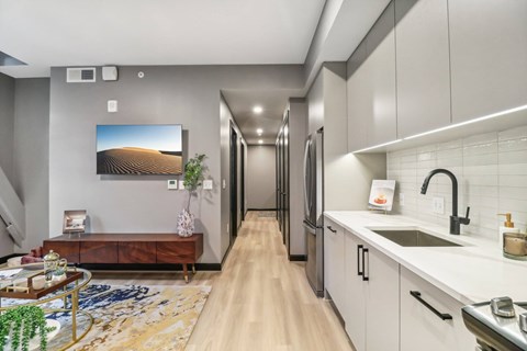 a kitchen with white cabinets and a long hallway with a tv on the wall