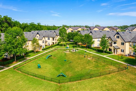 A large grassy field surrounded by a fence with houses in the background.