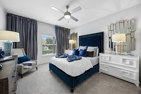 A bedroom with a large bed, a ceiling fan, and a window with curtains.