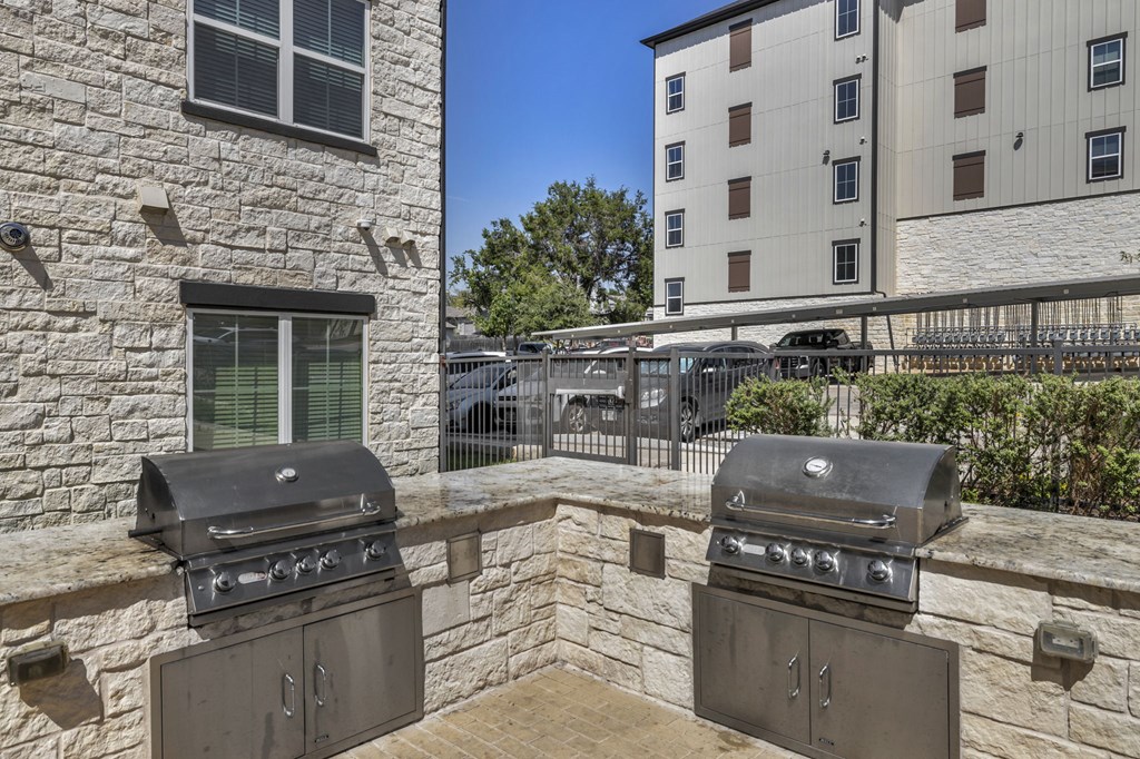 two gas grills on a stone patio with a building in the background