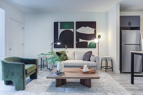 A living room with a green chair, a white couch, and a painting on the wall.