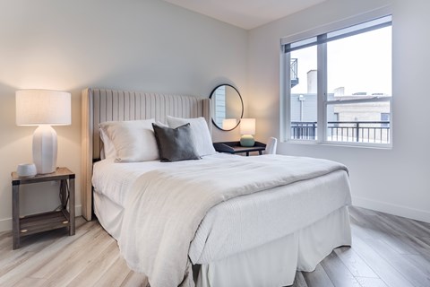 A bedroom with a large bed and a window overlooking a balcony.