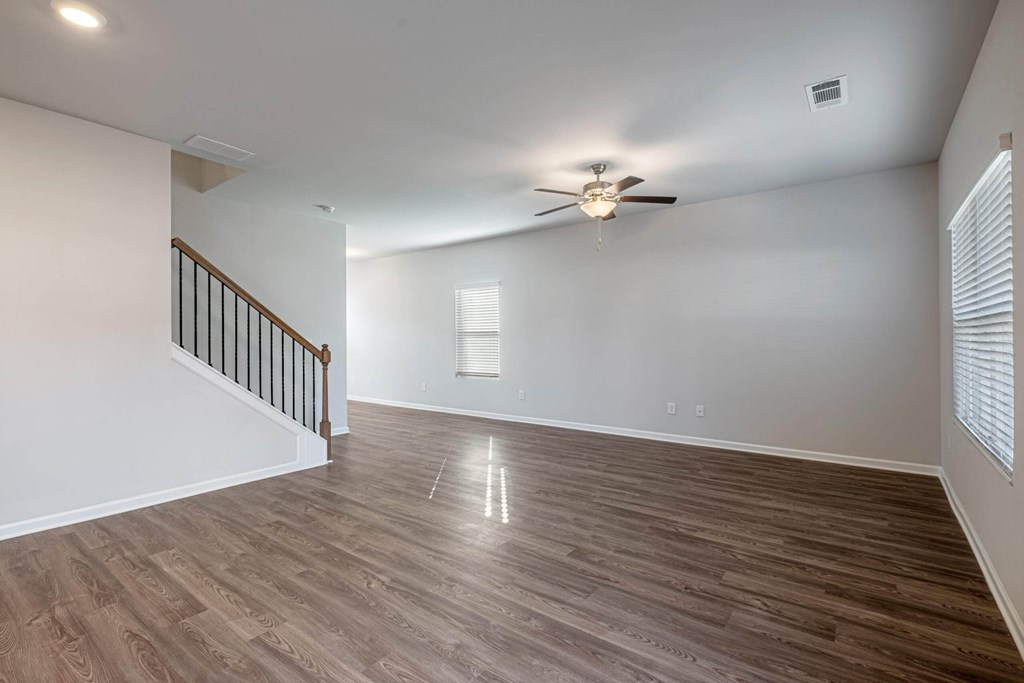 an empty living room with a ceiling fan and a staircase