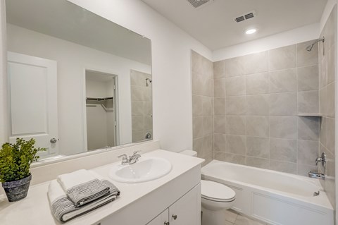 Well-lit bathroom with a garden tub adorned with tiled surroundings, accompanied by a large mirror, creating a bright and spacious ambiance for a comfortable bathing experience