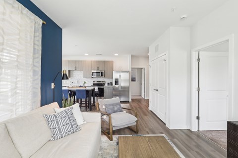 A modern living room with a white couch and a dining area in the background.