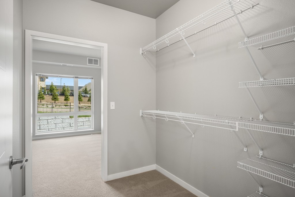 a spacious closet with shelves and hanging racks in a white room with a window