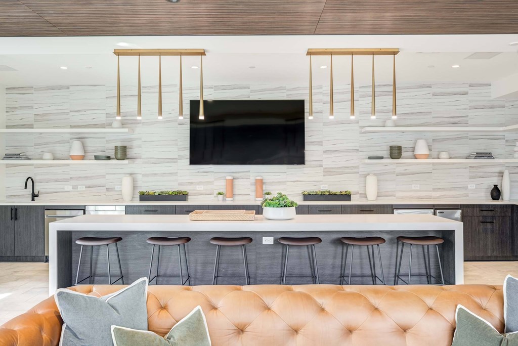 A modern kitchen with a bar and a brown leather sofa.