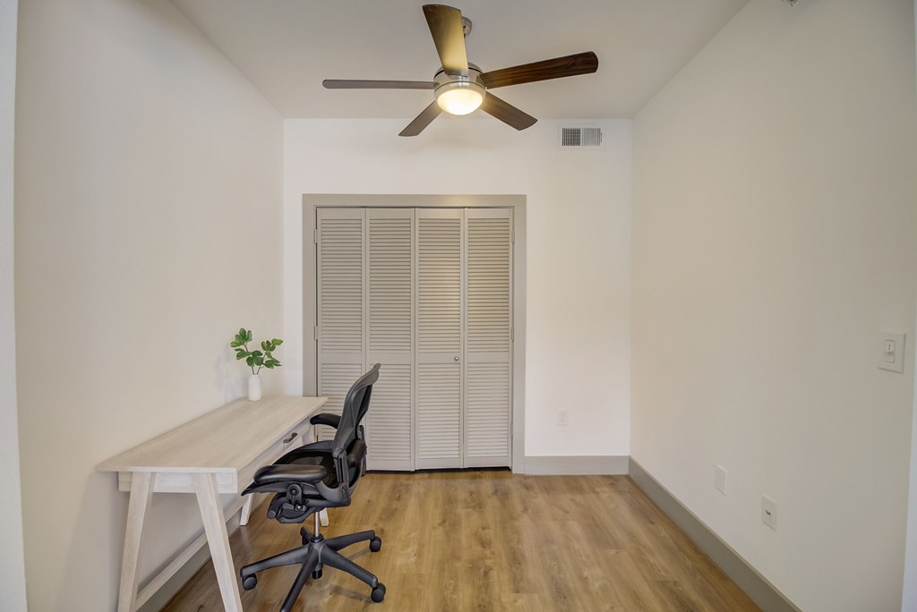a room with a desk and chair and a ceiling fan