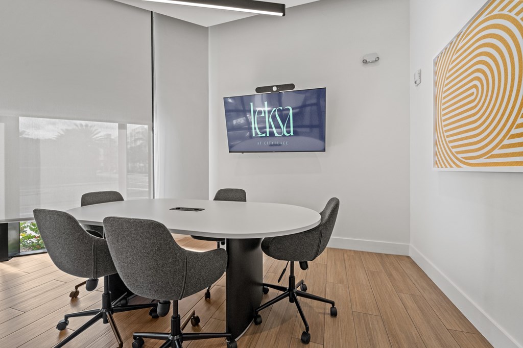 A conference room with a table, chairs, and a TV screen displaying the letters "ETKA".