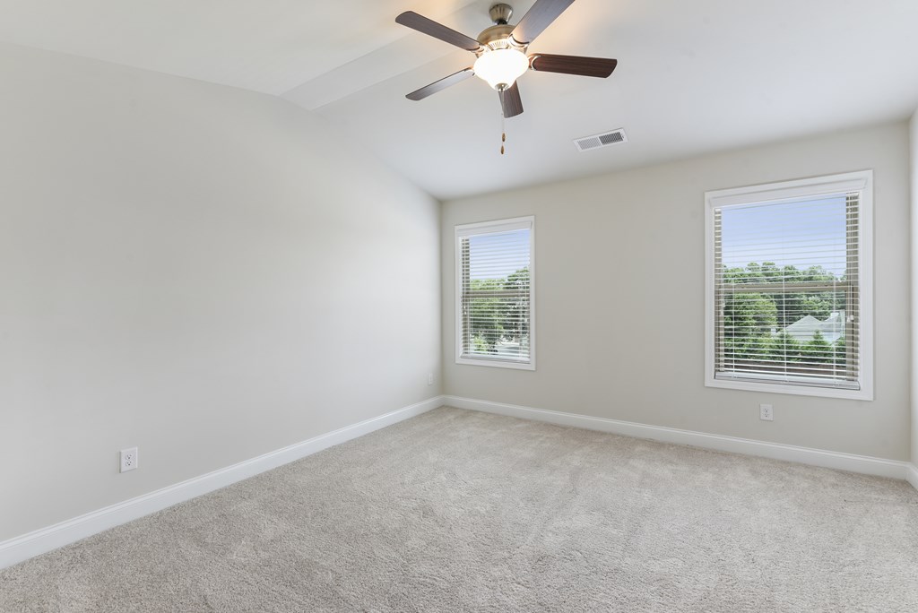 an empty living room with a ceiling fan and two windows
