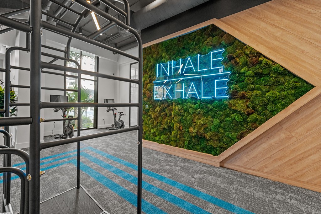 A gym with a green wall and a neon sign that says "NHALF EXHALE".