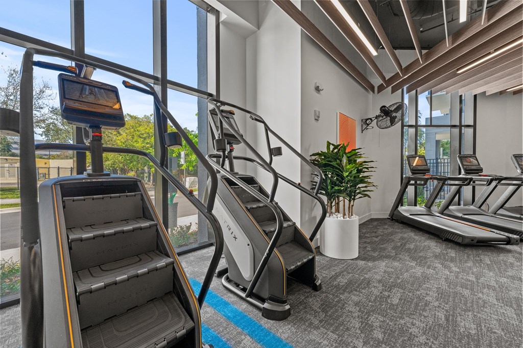 A treadmill and a stair climber are in a gym with a view of the outdoors.