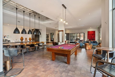 A billiard table is in the middle of a room with a kitchen area.