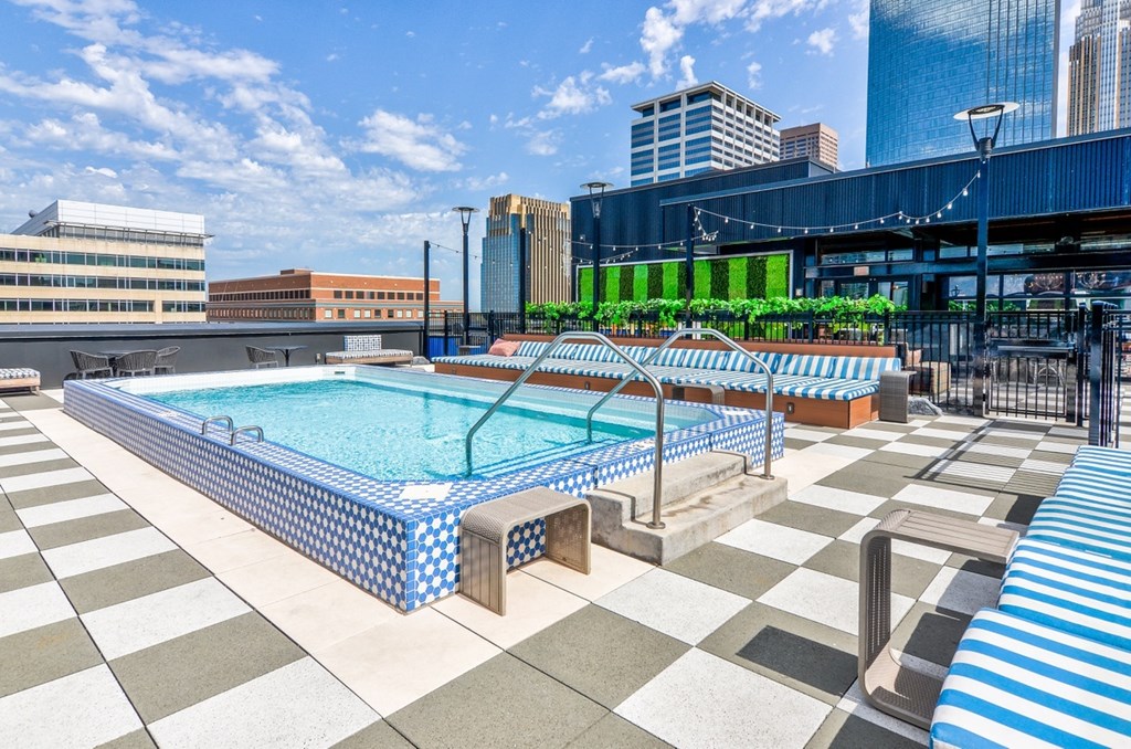 a rooftop pool with blue and white lounge chairs and a city skyline in the background