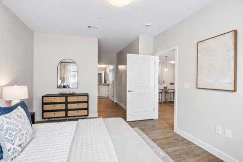 A bedroom with a white bed and a wooden dresser.