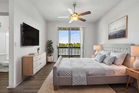 A bedroom with a large bed, a flat screen TV, and a balcony with a view of trees.