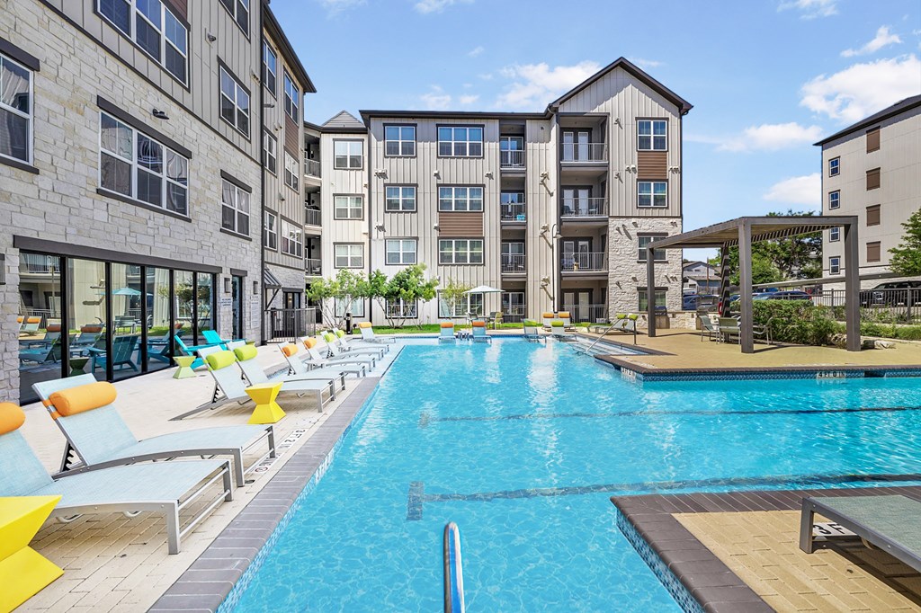 a swimming pool with lounge chairs in front of an apartment building