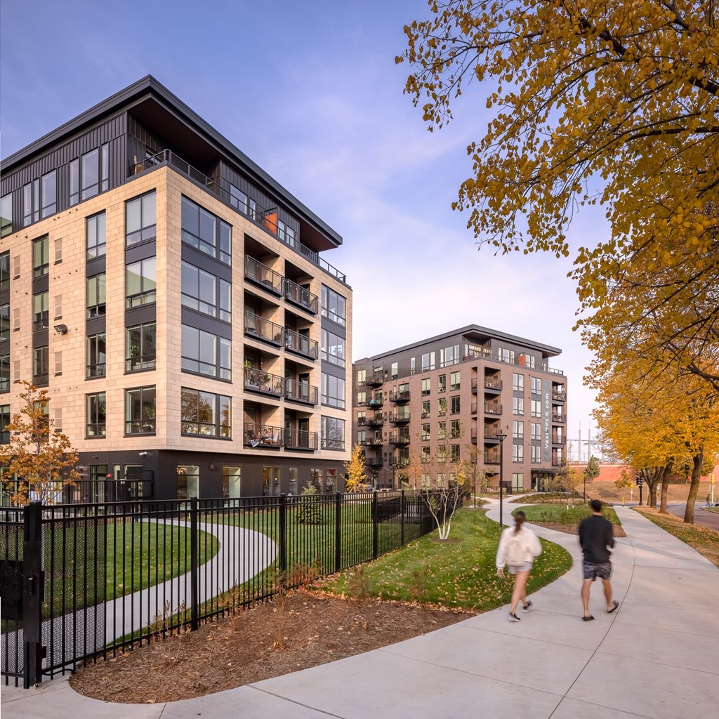 a man and a woman walking down a sidewalk in front of two apartment buildings