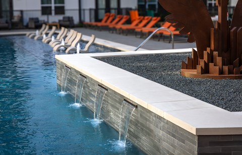 A pool with a waterfall feature and orange lounge chairs.