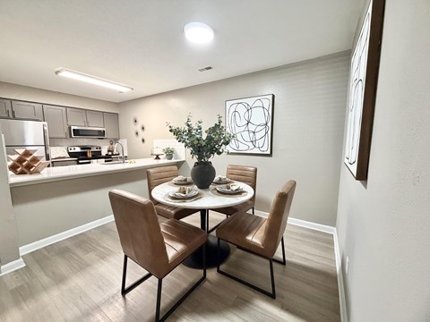 A dining room with a table set for two and a kitchen area in the background.