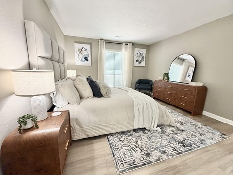 A bedroom with a large bed, a wooden nightstand, and a rug on the floor.