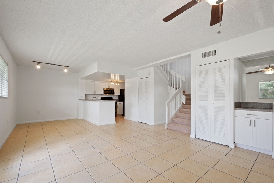 Open concept living, dining, and kitchen with ceiling fan and stairway to second floor