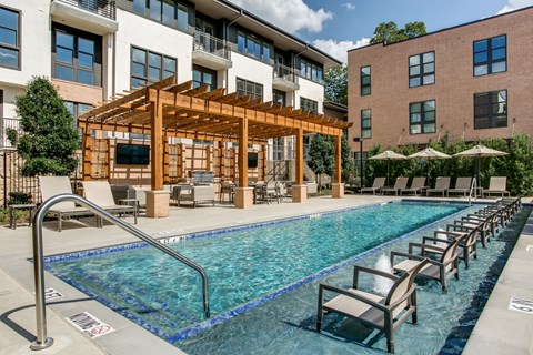 A pool area with a wooden structure and lounge chairs.