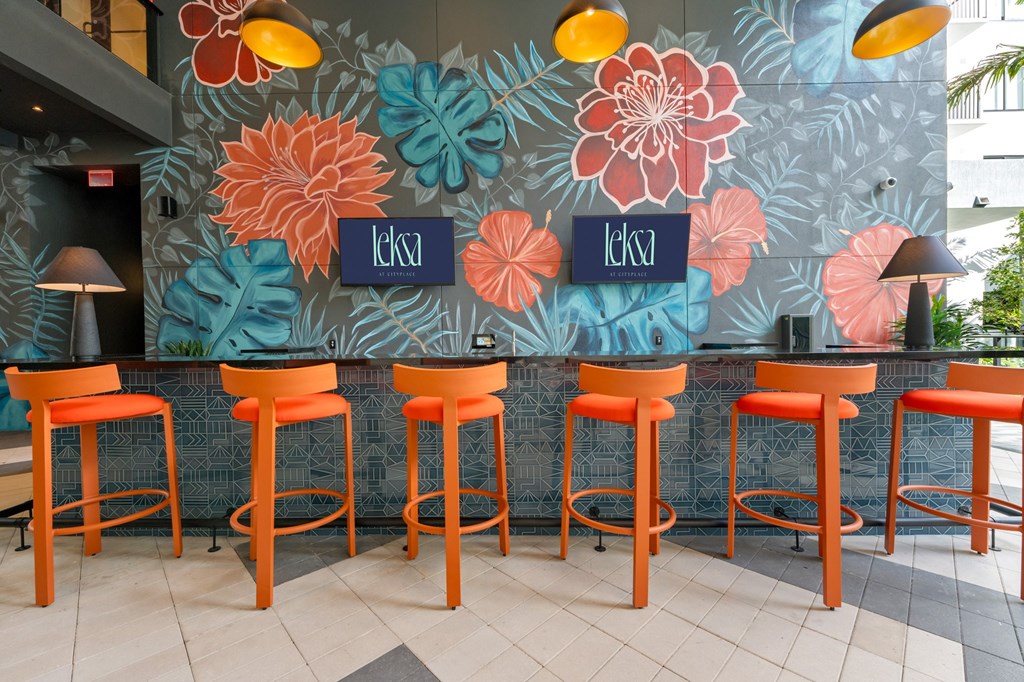 Outdoor bar with organge stools in front of a bar with a blue and green floral wallpaper and outdoor TV's.