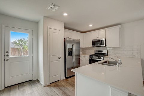 Kitchen featuring bright, white cabinets, well-lit to enhance the space. A door leading to the backyard not only provides access but also allows natural light to stream into the kitchen