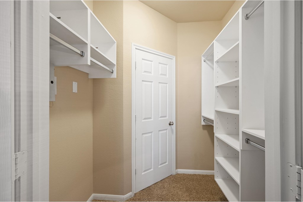 a walk in closet with white shelves and a closet door