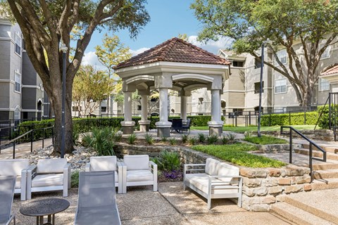 A gazebo is surrounded by white chairs and tables in a courtyard.