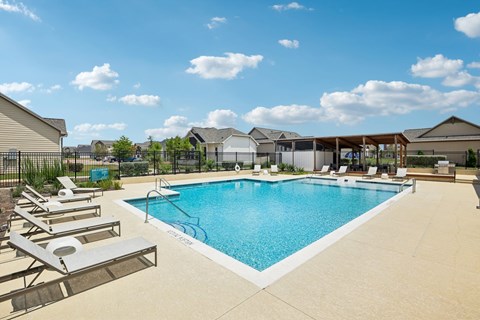 A large swimming pool with lounge chairs and a fence in the background.