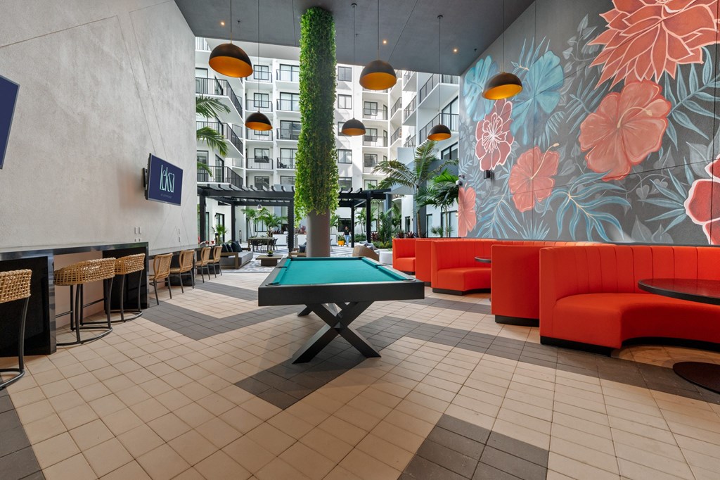 A pool table in the middle of a room with orange couches and a wall with a floral design.