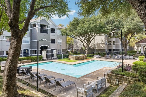 A swimming pool surrounded by trees and chairs in a residential area.