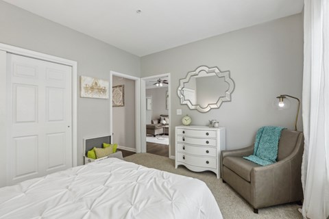 A bedroom with a white bed and a grey chair.