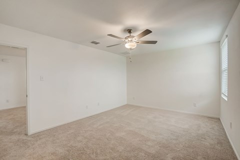 Generous bedroom space with carpet flooring and a central ceiling fan for added comfort and circulation.