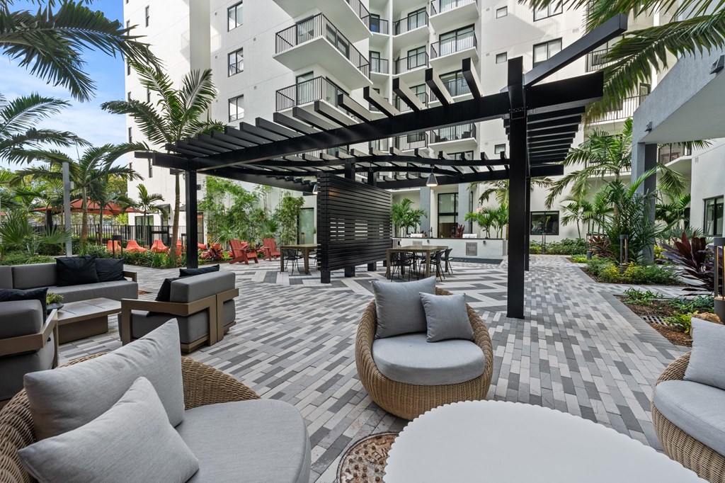 A patio with a black pergola and grey couches.