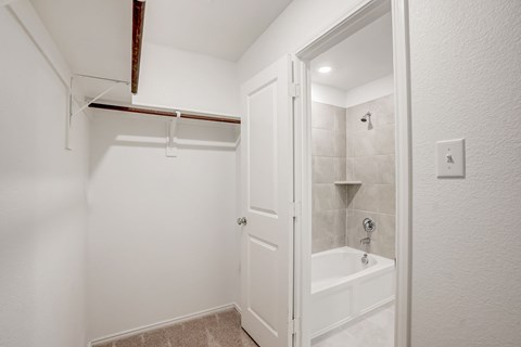 Bathroom with white cabinets, garden tub, a sizable mirror, and an attached walk-in closet, providing a functional and well-organized personal space.
